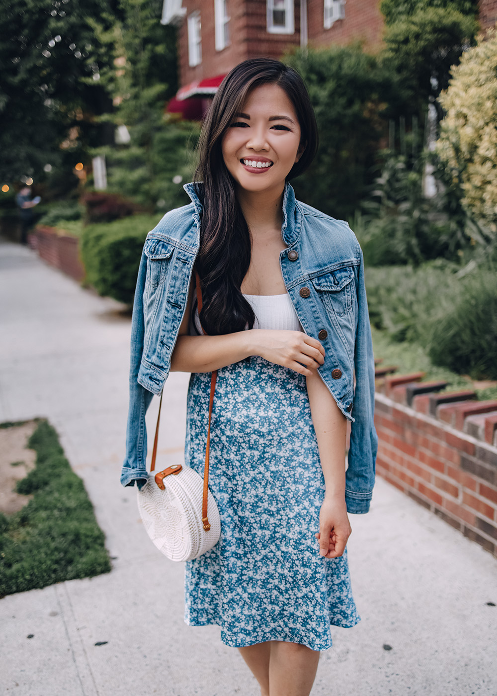 Casual Spring Outfit for Women: Denim Jacket, White Bodysuit, Blue Floral Midi Skirt, White Straw Circle Bag, White Leather Sneakers
